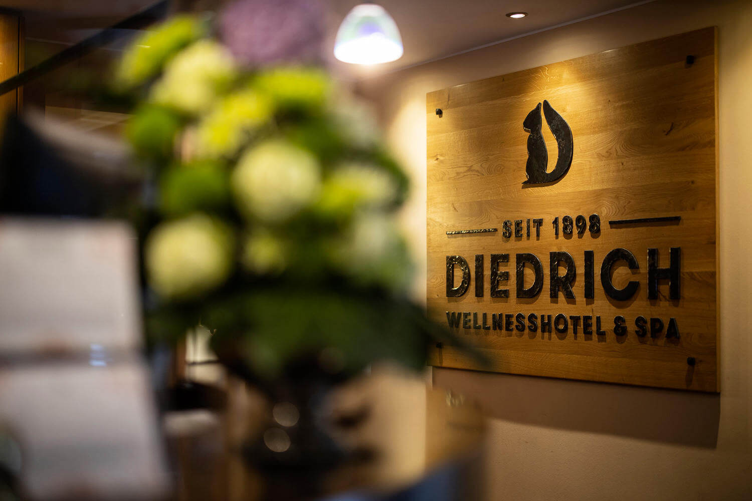 Large wooden plaque with the wrought-iron hotel logo at the reception of Hotel Diedrich