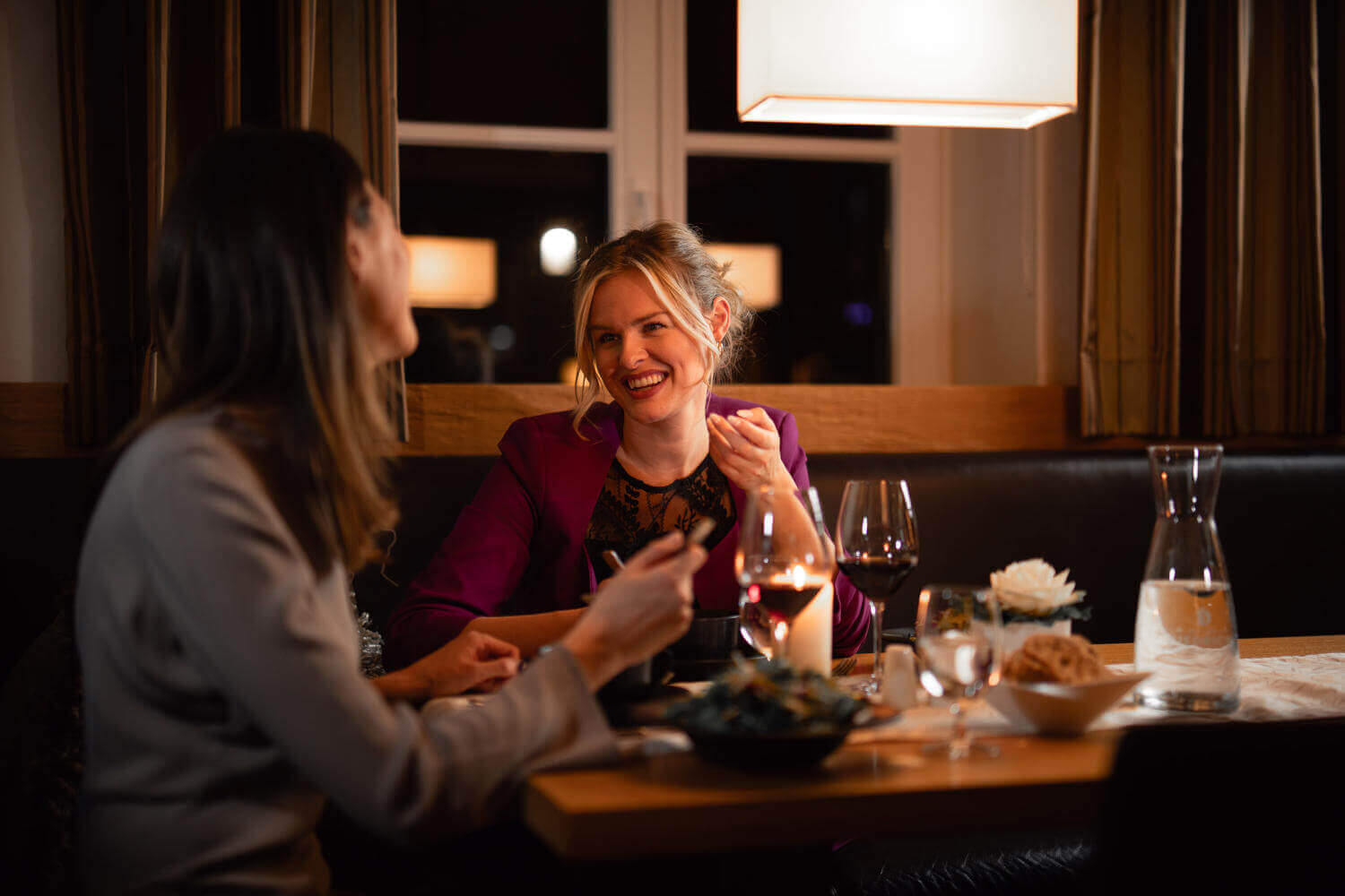 Zwei lächelnde Frauen beim Abendessen im gemütlichen Restaurant mit warmer Beleuchtung.