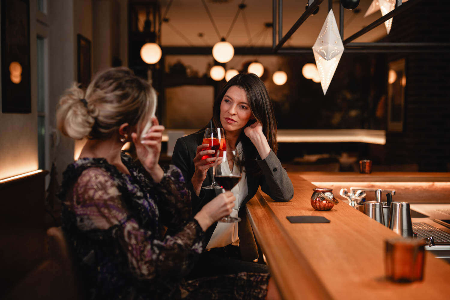 Zwei Frauen genießen Getränke und eine entspannte Unterhaltung an der Bar des stilvollen Restaurants bei Abendbeleuchtung.