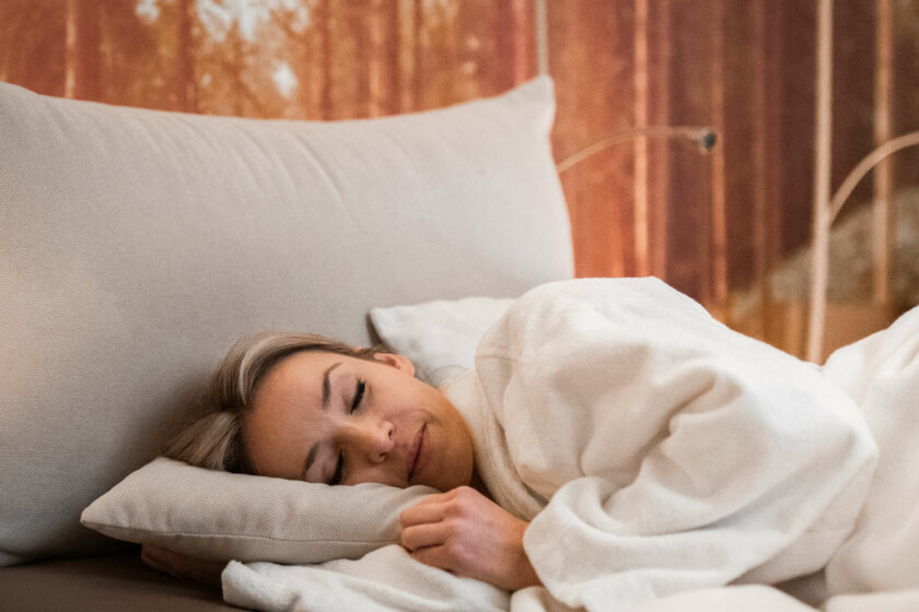 Eine Frau liegt seitlich eingekuschelt auf einem Bett im Ruhebereich des Wellnesshotels und schläft.