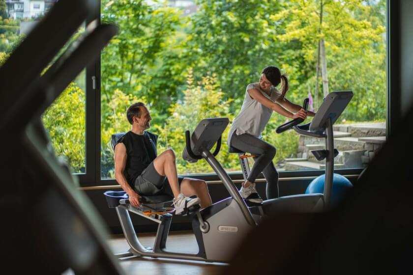 Paar trainiert im Fitnessbereich des Wellnesshotels Diedrich im Sauerland mit Blick auf die grüne Landschaft